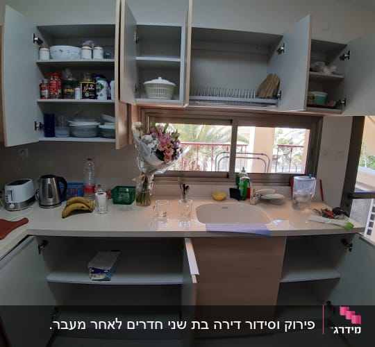 מטבח עם ארונות פתוחים, כלים ומוצרי ניקוי על השיש